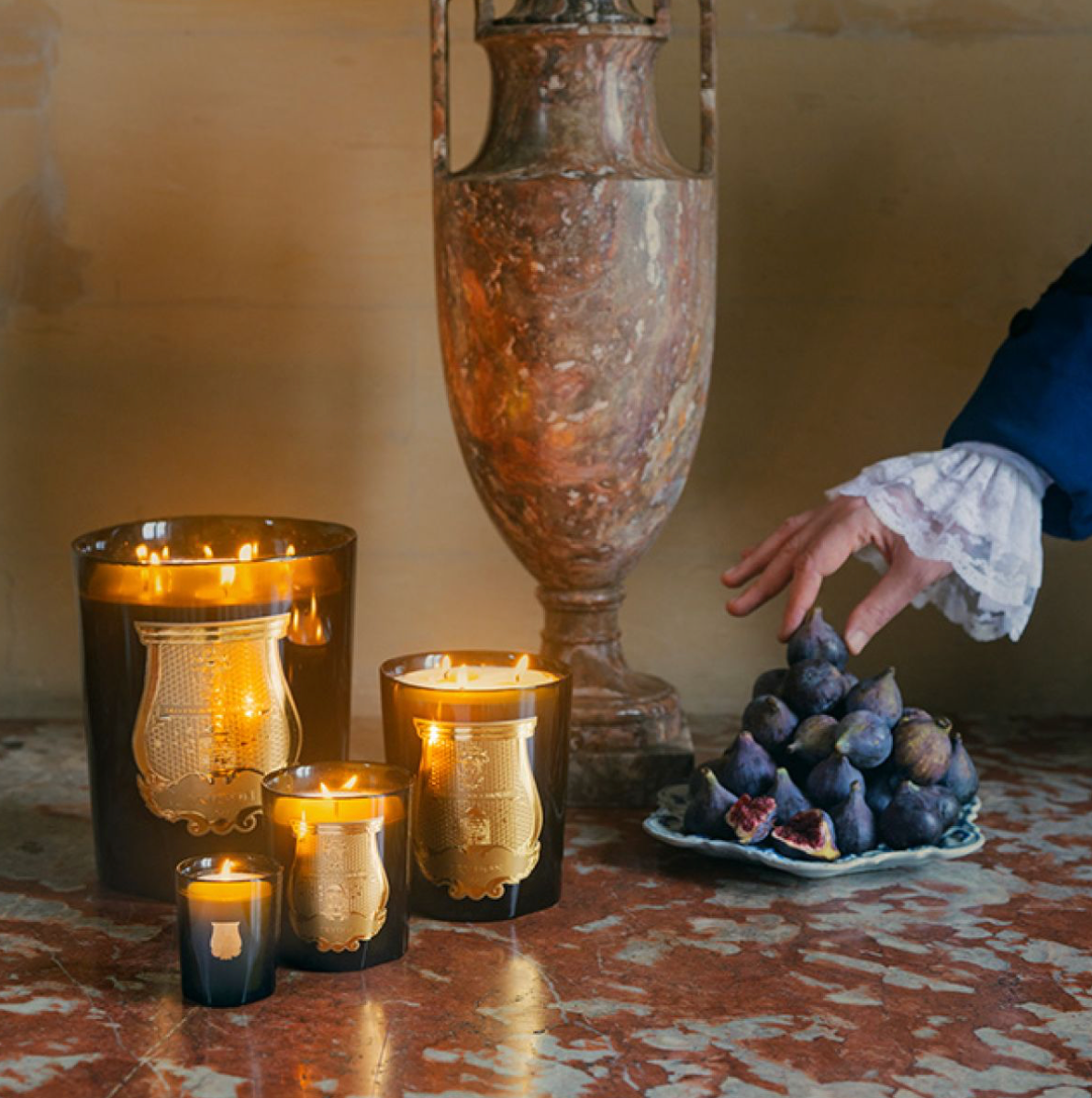 Set of lit Trudon Cyrnos candles in black glass holders with gold emblems, creating warm ambiance, SKU: 3003730049