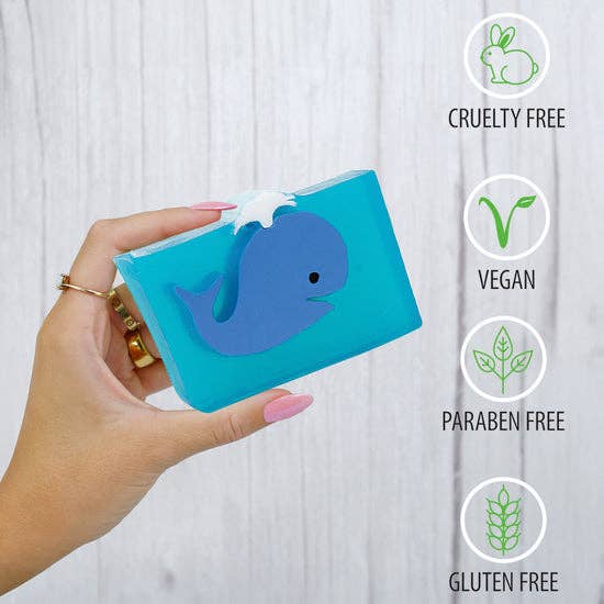 Hand holding blue whale glycerin soap with eco-friendly icons indicating cruelty-free, vegan, paraben-free, and gluten-free