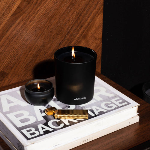 Close-up of a black charcoal mini candle on a wooden surface with a textured background, highlighting the candle's sleek design