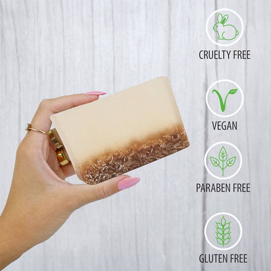 Hand holding rectangular lavender oatmeal soap with brown oatmeal layer, showing cruelty-free, vegan, paraben-free, gluten-free icons