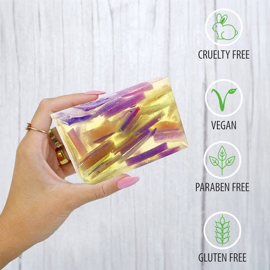 Hand holding a rectangular patchouli soap with purple and yellow swirls, cruelty-free, vegan, paraben-free, gluten-free icons