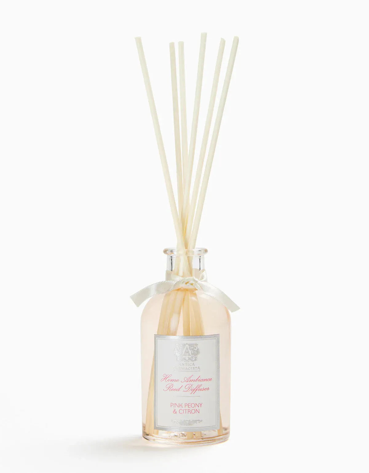 Elegant glass reed diffuser bottle with cream-colored reeds, tied with a satin ribbon, labeled with pink peony scent for home fragrance