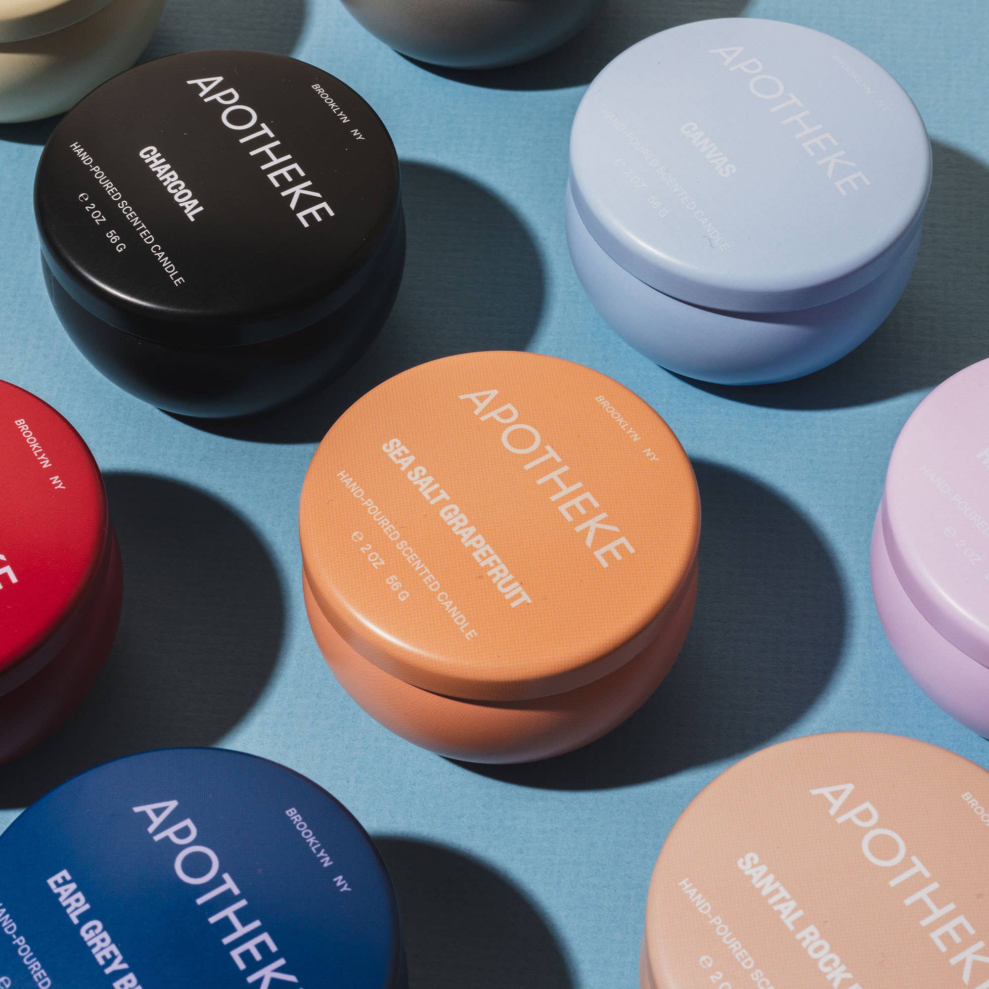 Black and white candle containers with simple text, placed on a blue surface, showcasing different scents and packaging styles